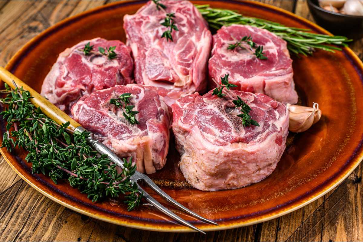 cuts of lamb neck arranged on an earthenware plate and garnished with fresh herbs on the side